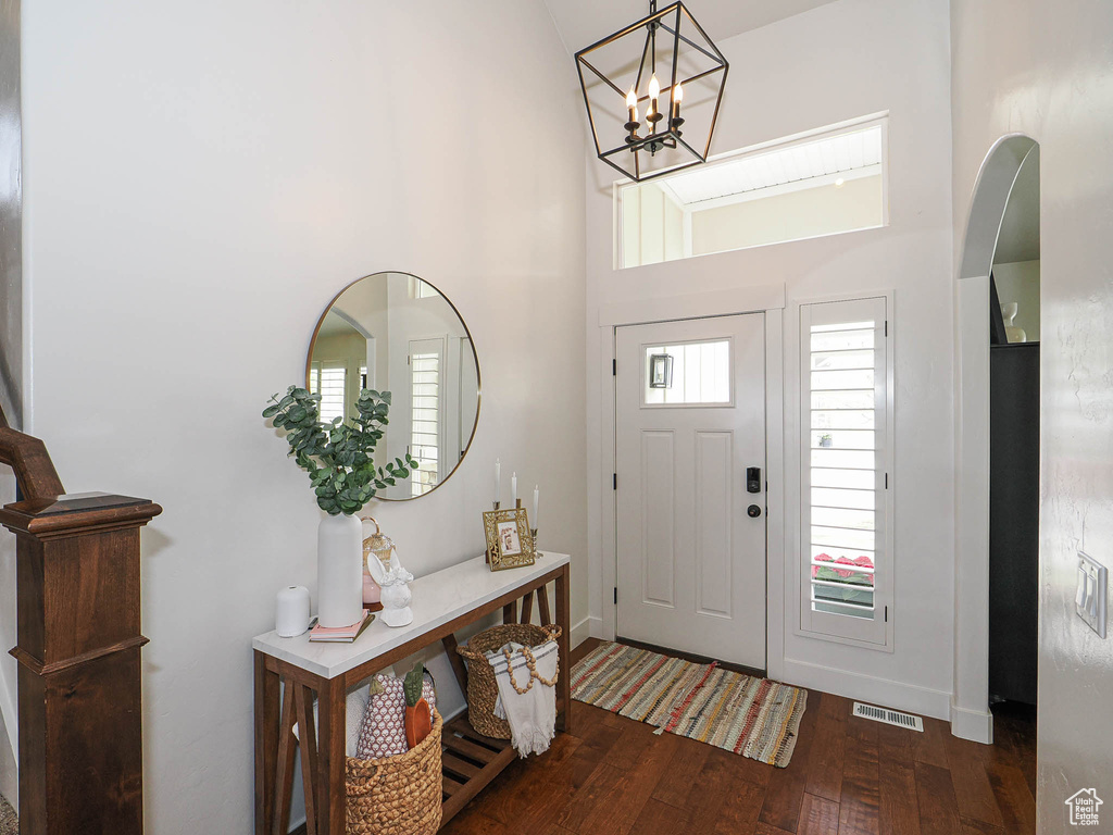 Foyer entrance with a towering ceiling, visible vents, a healthy amount of sunlight, hardwood / wood-style flooring, and a notable chandelier