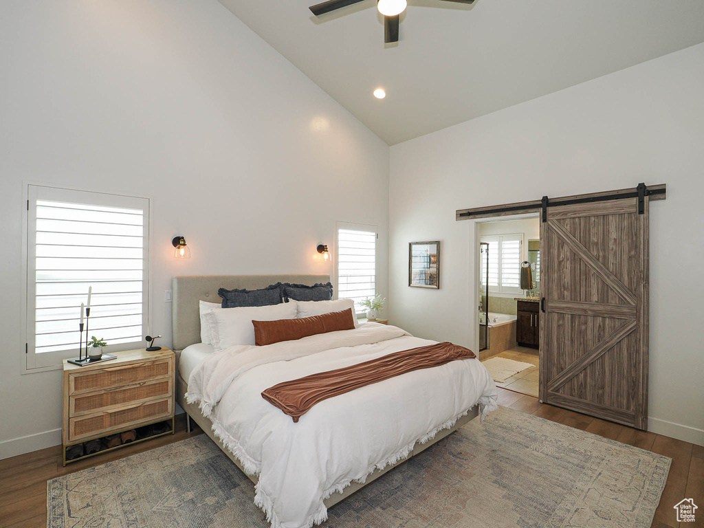 Bedroom featuring a barn door, wood finished floors, baseboards, high vaulted ceiling, and ensuite bathroom
