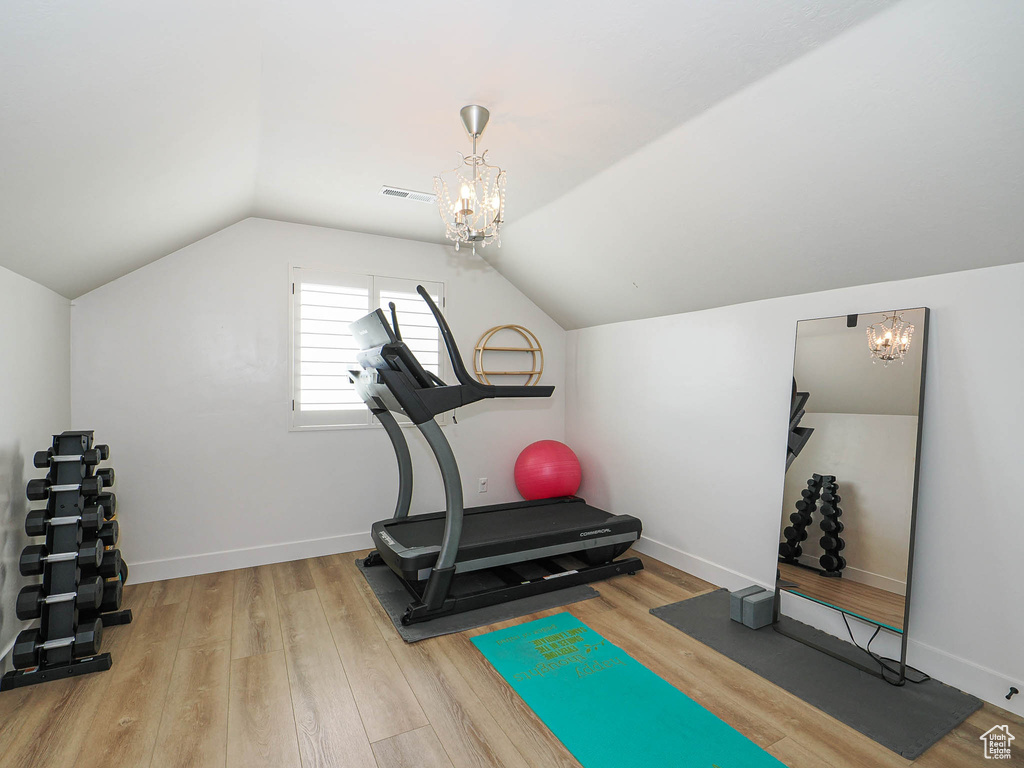 Workout area with a chandelier, vaulted ceiling, wood finished floors, and visible vents