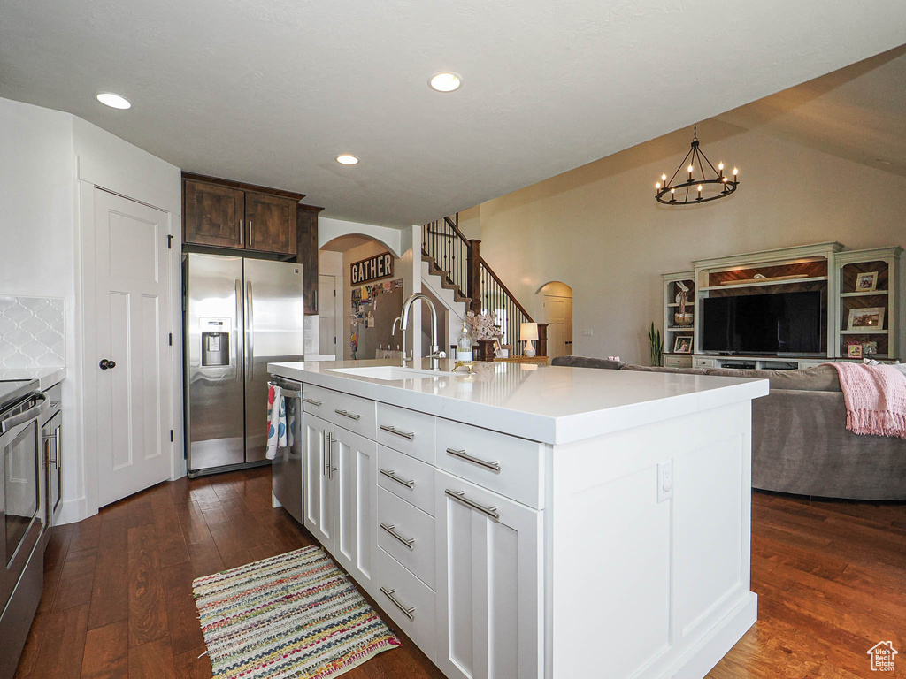 Kitchen featuring a sink, arched walkways, appliances with stainless steel finishes, a notable chandelier, and dark wood-type flooring