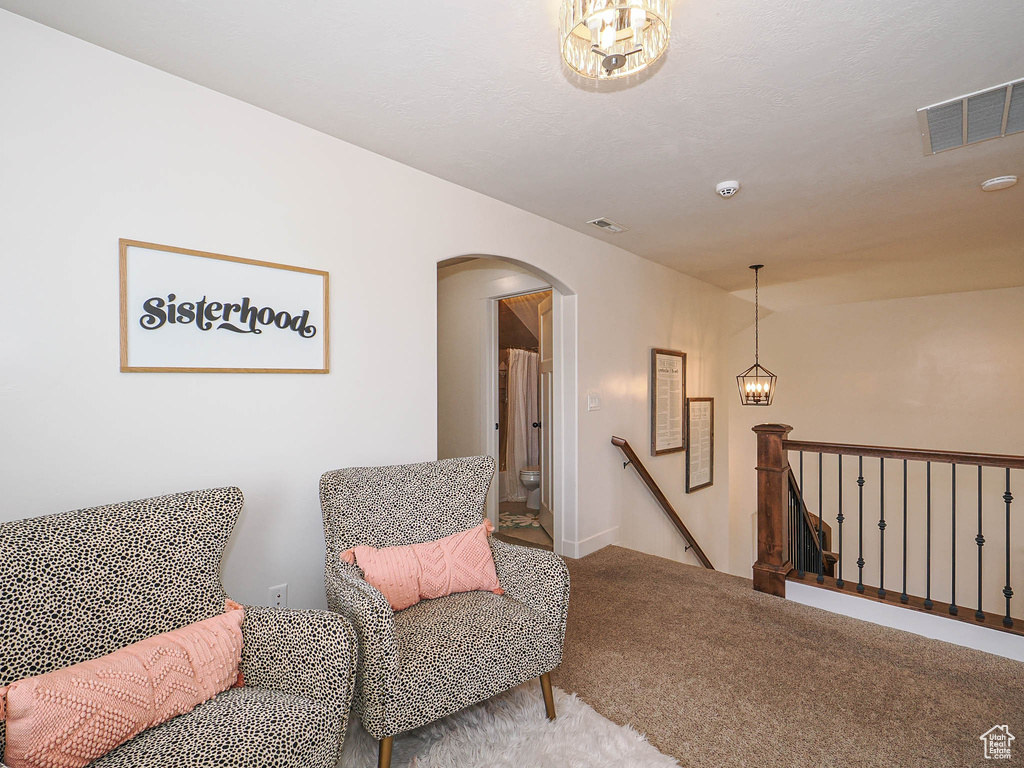 Sitting room with an upstairs landing, arched walkways, carpet floors, a notable chandelier, and visible vents