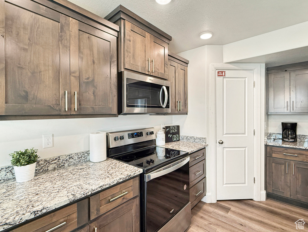 Kitchen with a textured ceiling, light wood-style flooring, light stone countertops, and appliances with stainless steel finishes