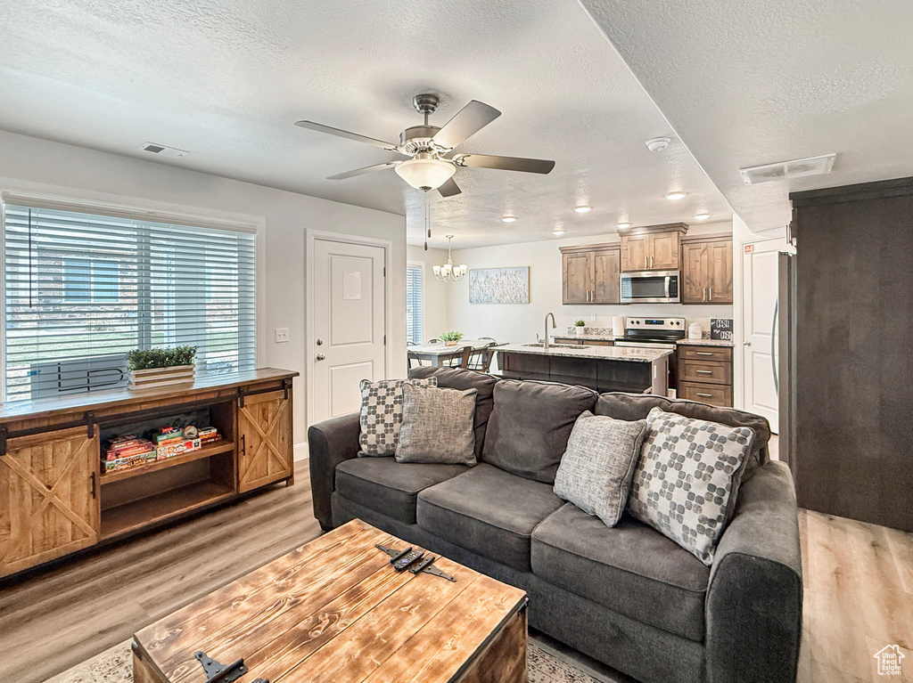 Living area featuring a textured ceiling, ceiling fan with notable chandelier, visible vents, and light wood-style flooring