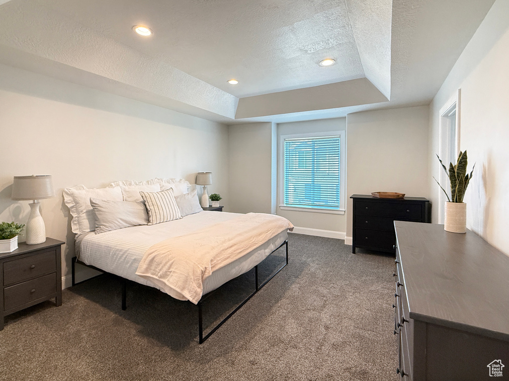 Bedroom featuring a textured ceiling, a tray ceiling, baseboards, dark colored carpet, and recessed lighting