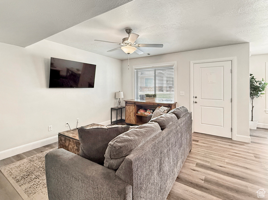 Living room with light wood-type flooring, a textured ceiling, baseboards, and ceiling fan