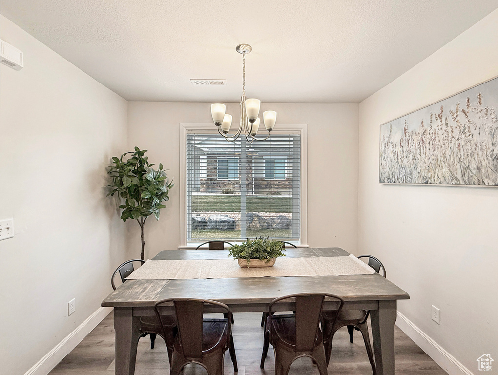 Dining room with visible vents, baseboards, wood finished floors, and an inviting chandelier
