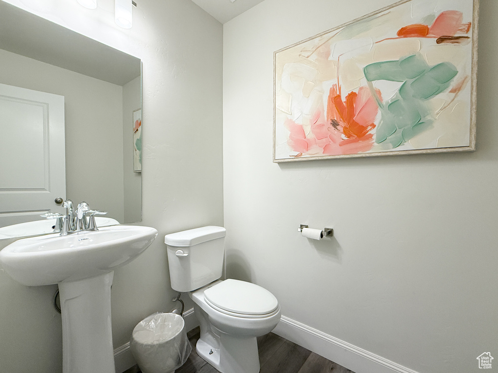 Bathroom featuring baseboards, wood finished floors, a sink, and toilet