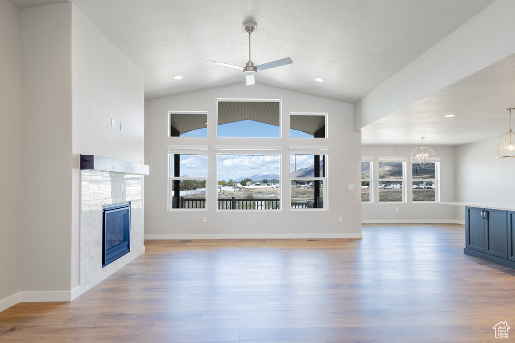 Unfurnished living room featuring recessed lighting, a glass covered fireplace, light wood-style floors, and ceiling fan with notable chandelier