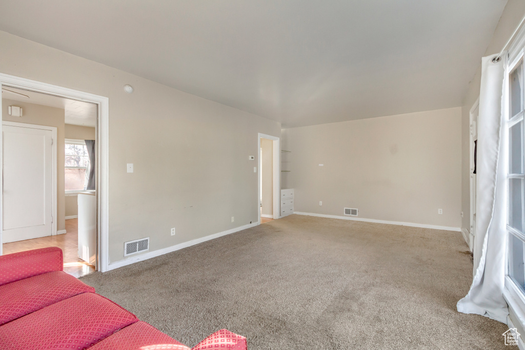 Unfurnished living room with visible vents, carpet flooring, and baseboards