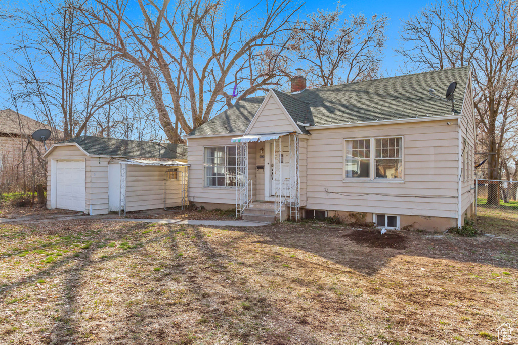 View of front of home featuring fence, roof with shingles, a chimney, and an outbuilding