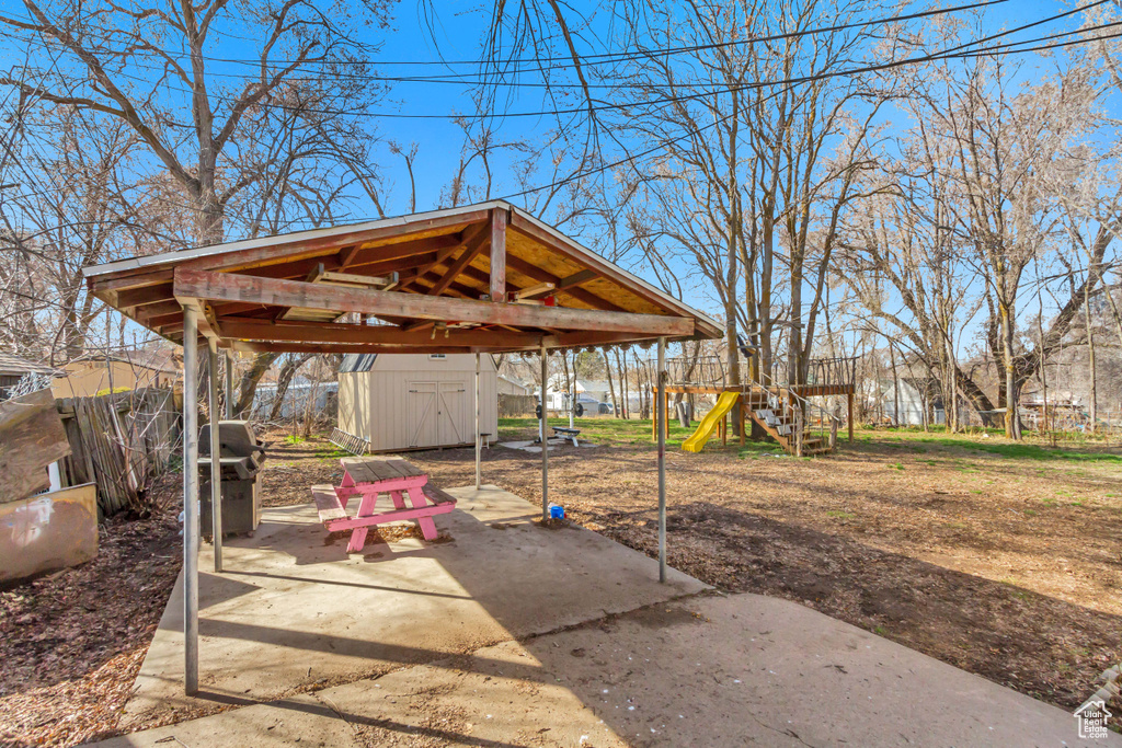 View of patio featuring an outdoor structure, a playground, a gazebo, a shed, and fence