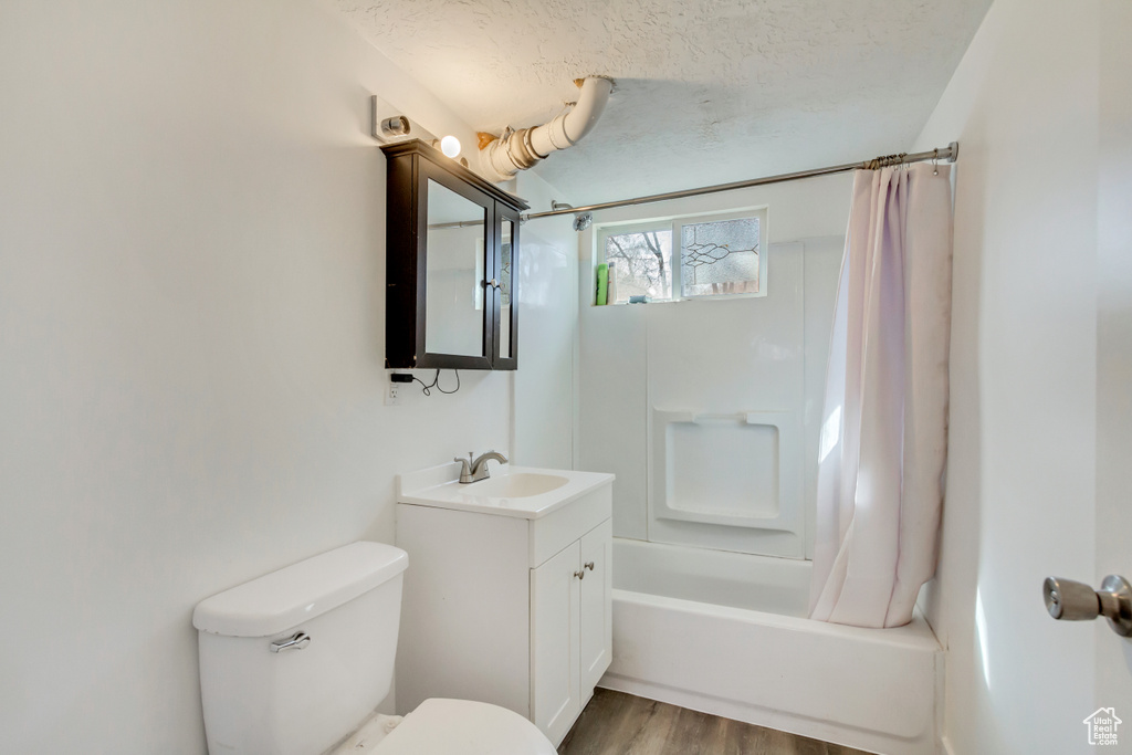 Bathroom featuring vanity, shower / bath combination with curtain, toilet, a textured ceiling, and wood finished floors