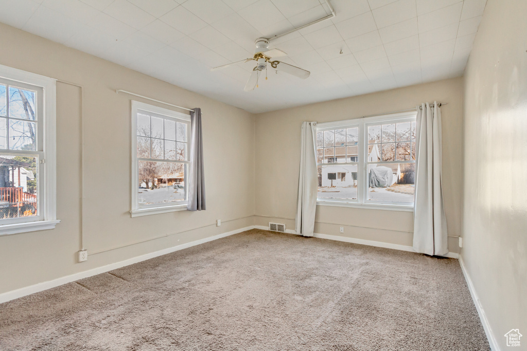 Empty room with visible vents, a ceiling fan, and carpet flooring