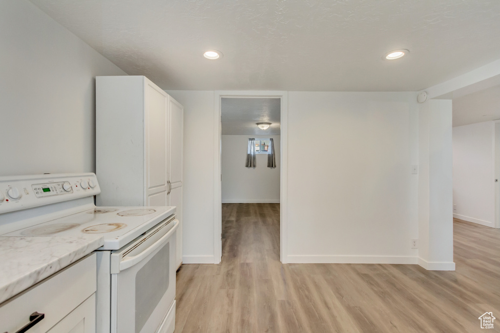 Kitchen with white cabinetry, baseboards, white electric stove, and light wood-style floors