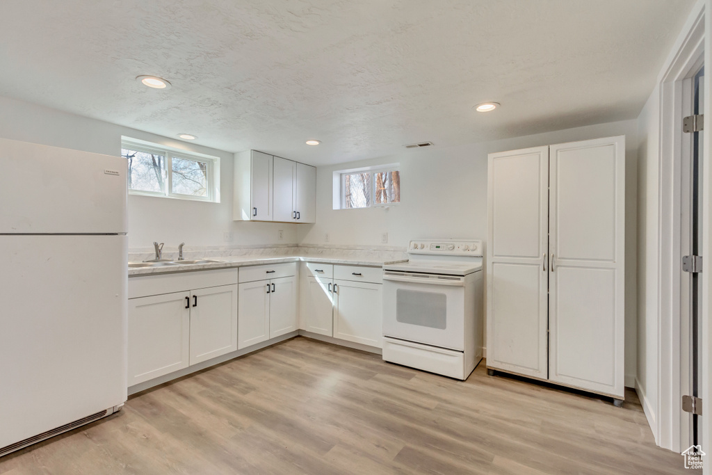 Kitchen featuring white cabinetry, a sink, visible vents, light wood-type flooring, and white appliances
