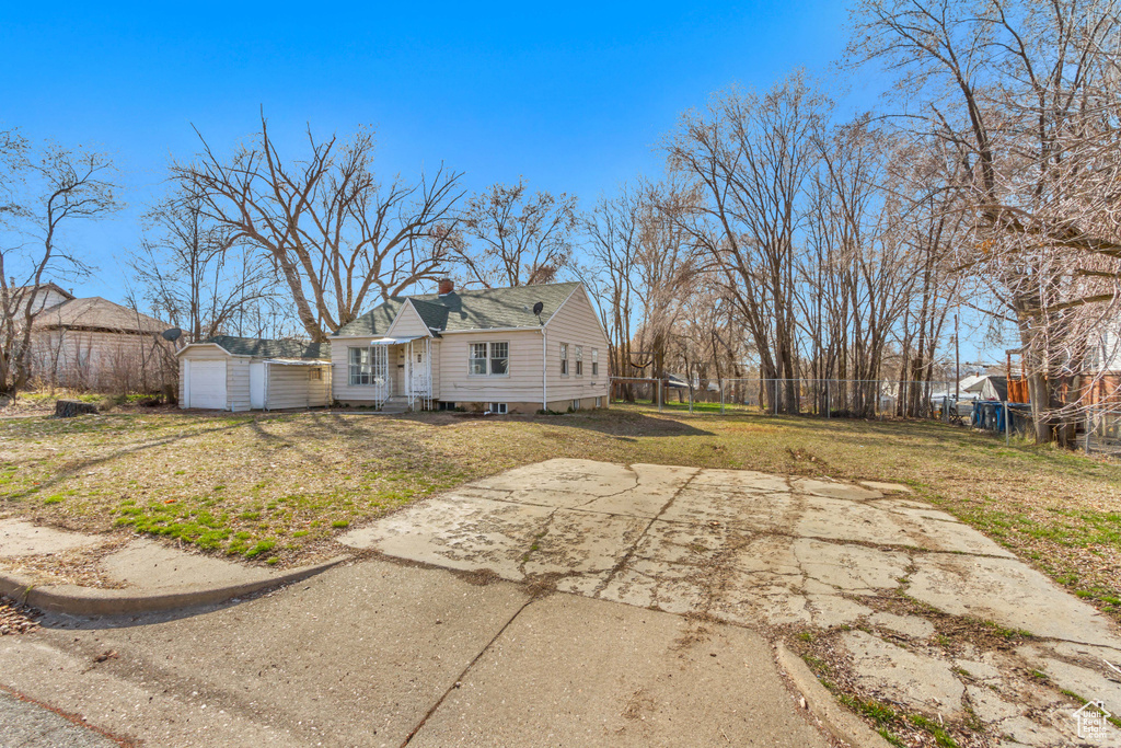 View of side of property featuring a chimney, fence, an outbuilding, a detached garage, and a lawn
