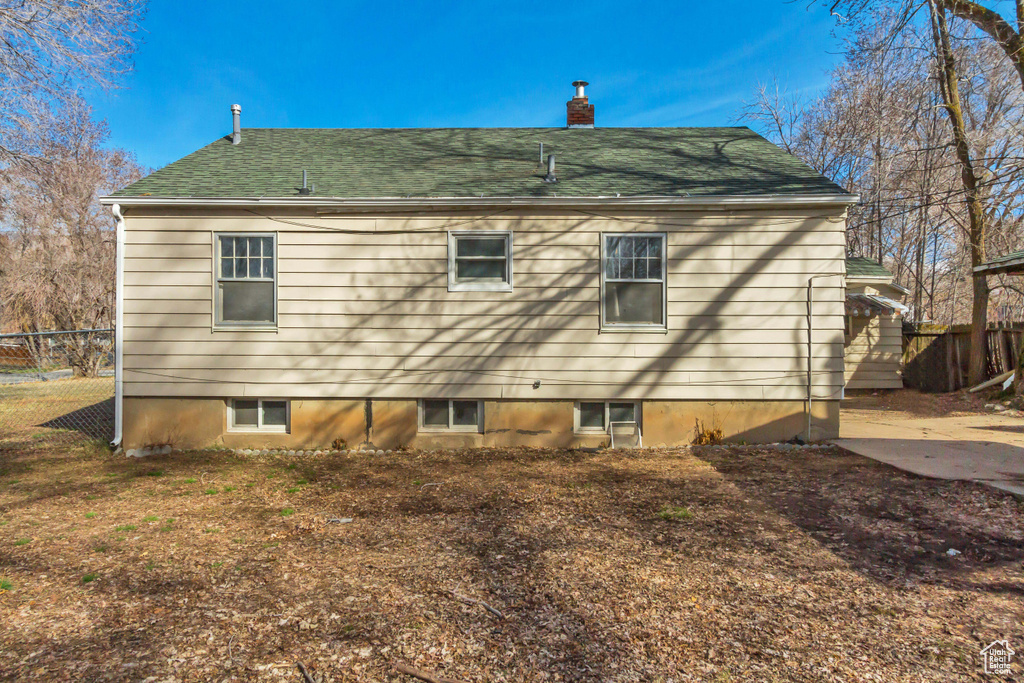 Back of house with fence, a chimney, and a shingled roof