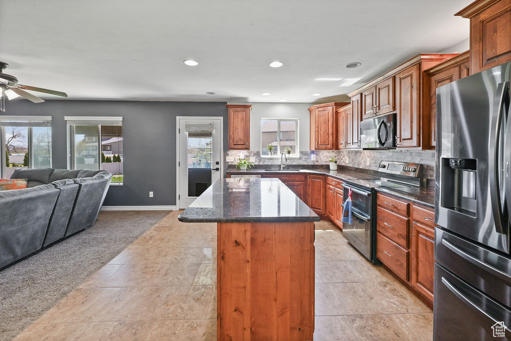 Kitchen featuring stainless steel appliances, backsplash, a kitchen island, open floor plan, and ceiling fan