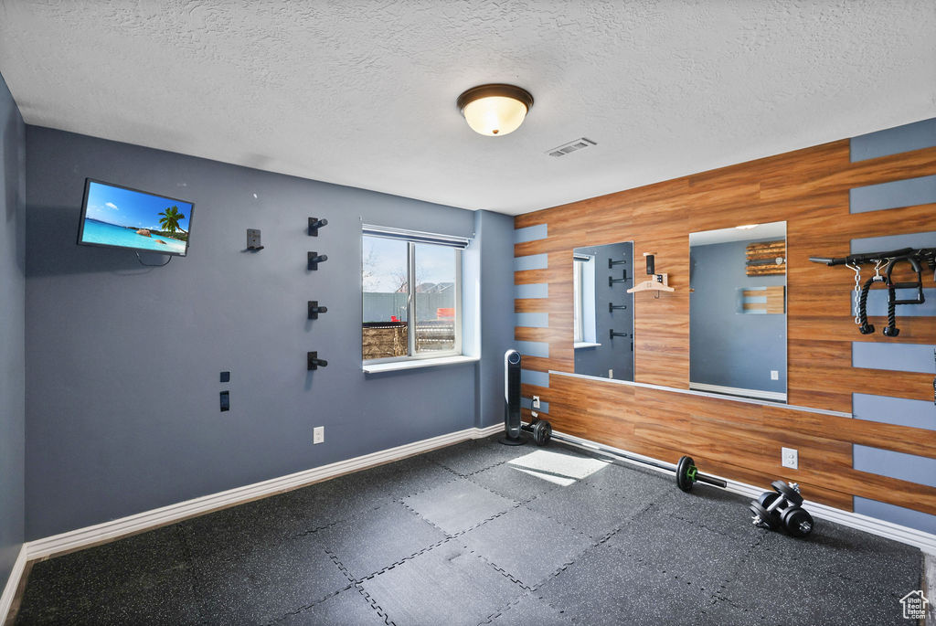 Workout area with visible vents, baseboards, wood walls, and a textured ceiling