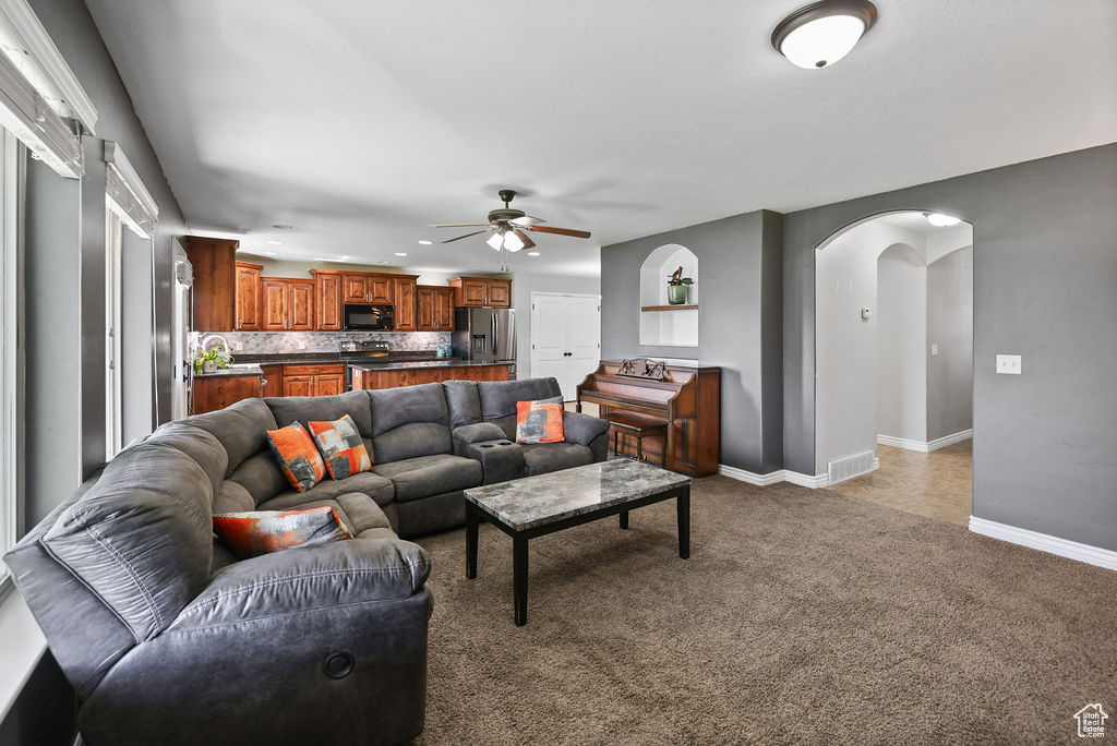 Carpeted living area featuring arched walkways, visible vents, baseboards, recessed lighting, and a ceiling fan