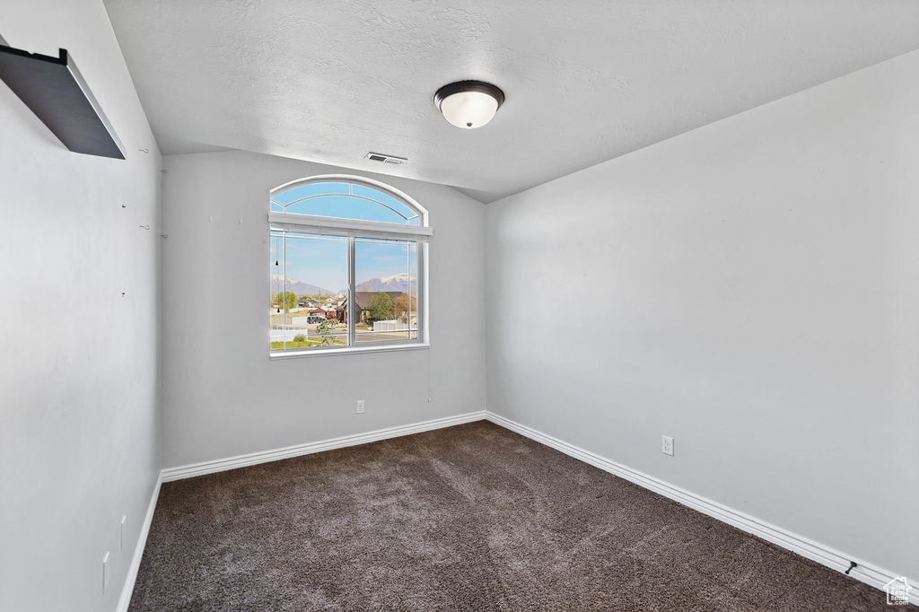 Spare room featuring dark colored carpet, a textured ceiling, baseboards, and visible vents