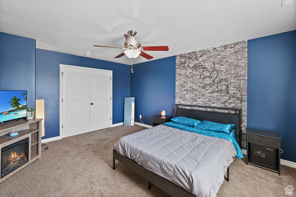 Bedroom featuring a closet, baseboards, a glass covered fireplace, carpet flooring, and ceiling fan
