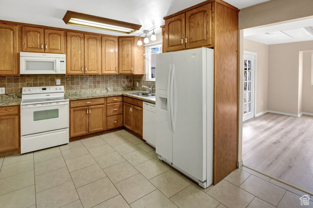 Kitchen with tasteful backsplash, light stone countertops, white appliances, brown cabinets, and a sink