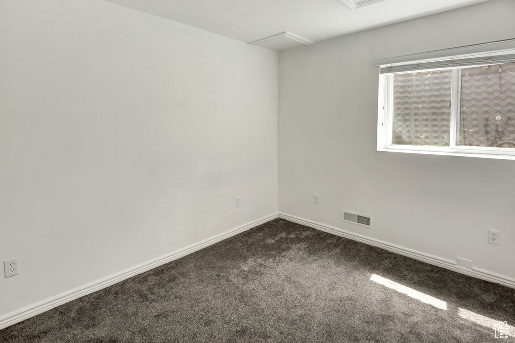 Unfurnished room featuring baseboards, visible vents, and dark carpet