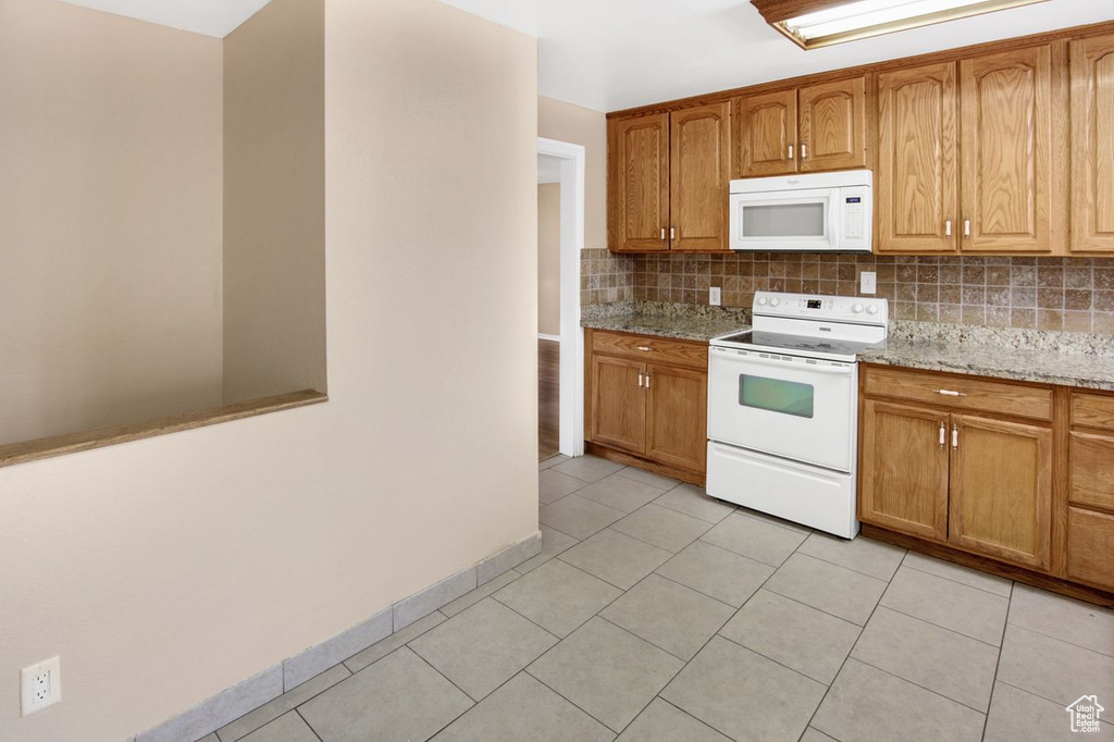 Kitchen featuring light tile patterned flooring, backsplash, light stone countertops, and white appliances