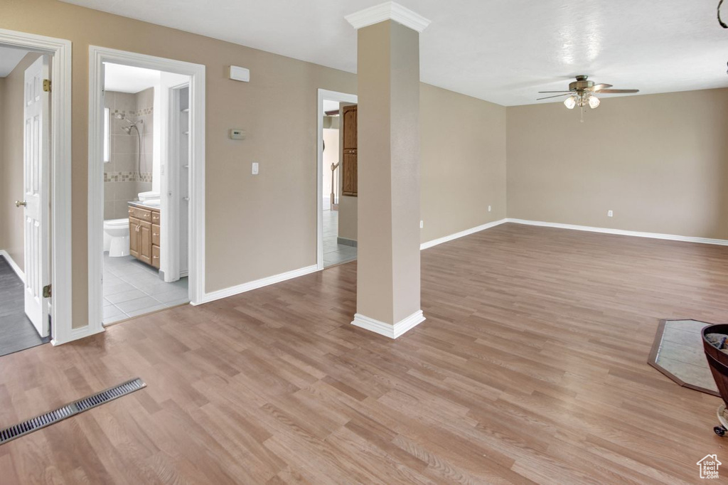 Unfurnished living room with light wood finished floors, ornate columns, ceiling fan, and baseboards