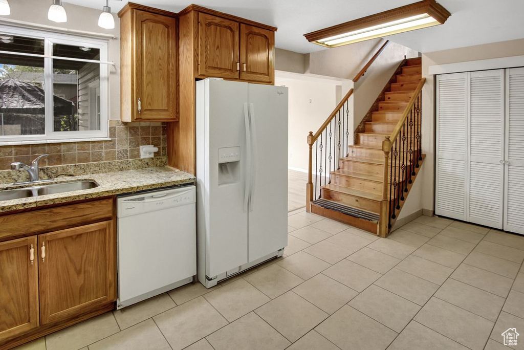 Kitchen featuring decorative backsplash, a sink, light stone countertops, white appliances, and brown cabinetry
