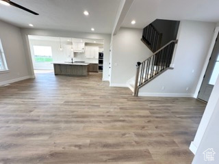 Unfurnished living room with baseboards, stairway, light wood-style flooring, and recessed lighting