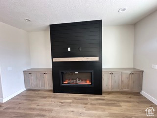 Unfurnished living room featuring a textured ceiling, baseboards, wood finished floors, and a glass covered fireplace