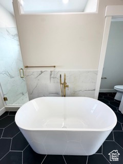 Full bathroom featuring a freestanding tub, a shower stall, wainscoting, and tile walls