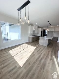 Kitchen with open floor plan, white cabinetry, light wood finished floors, and baseboards