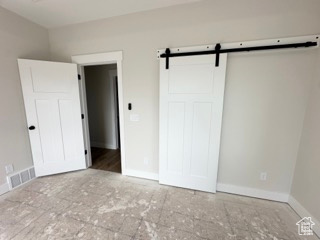 Unfurnished bedroom featuring visible vents, a barn door, and baseboards