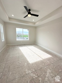 Unfurnished room with a ceiling fan, baseboards, and a tray ceiling