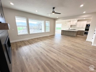 Unfurnished living room with baseboards, a ceiling fan, light wood-type flooring, and a large fireplace