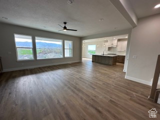 Unfurnished living room featuring baseboards, a ceiling fan, and dark wood-style flooring