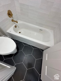 Bathroom with tile walls, tile patterned flooring, toilet, and a bathing tub