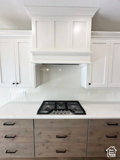 Kitchen featuring white cabinets, light stone countertops, and stainless steel gas stovetop