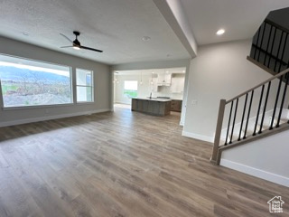 Unfurnished living room featuring recessed lighting, a ceiling fan, stairs, baseboards, and wood finished floors