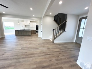 Unfurnished living room with baseboards, stairway, a wealth of natural light, and recessed lighting