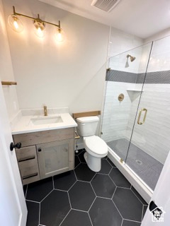 Bathroom featuring tile patterned flooring, toilet, vanity, visible vents, and a stall shower