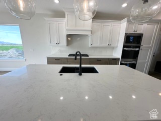 Kitchen featuring white cabinetry, a sink, stovetop, light stone countertops, and stainless steel oven