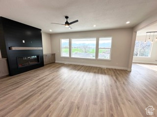 Unfurnished living room featuring recessed lighting, a glass covered fireplace, a ceiling fan, baseboards, and wood finished floors