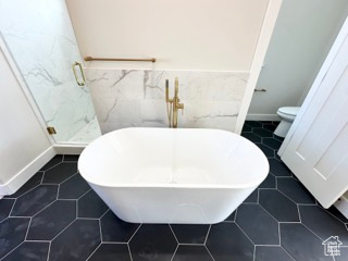 Full bathroom featuring toilet, a soaking tub, a stall shower, and wainscoting