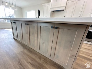 Kitchen with light countertops, pendant lighting, white cabinets, and light wood-type flooring