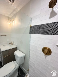 Full bath with toilet, a tile shower, visible vents, and vanity