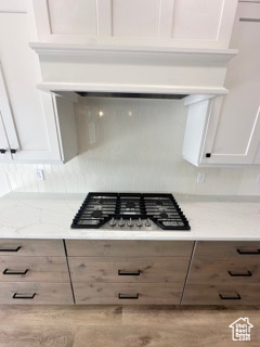 Details with white cabinets, light stone countertops, stainless steel gas stovetop, and premium range hood